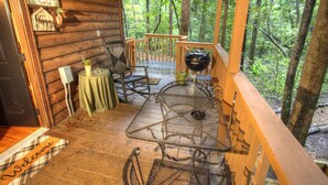 Une cabane en bois avec une véranda, une table en métal, des chaises et un paillasson.