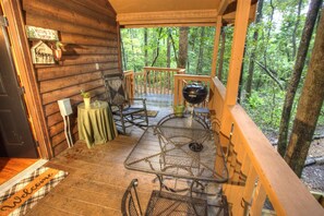 Een houten chalet met een veranda, een metalen tafel, stoelen en een welkomstmat.