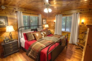 A wooden cabin bedroom with a bed, nightstands, a dresser, and a ceiling fan.