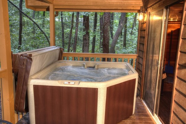 A hot tub with a wooden exterior, surrounded by a wooden deck and a forest view.