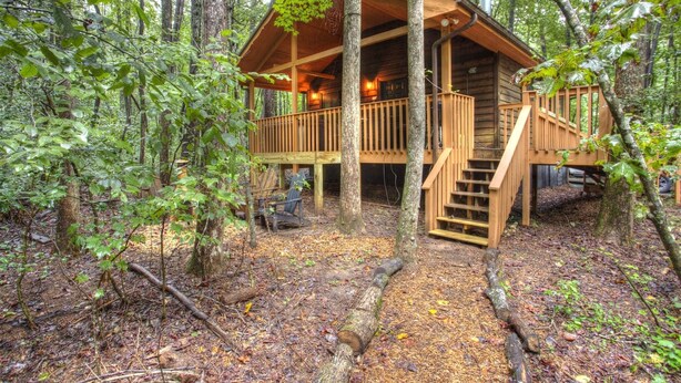 Une cabane en bois dotée d’une terrasse et d’un escalier, entourée d’arbres.