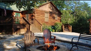A wooden cabin with a stone fire pit, a covered porch, and a staircase leading to the entrance. - Hutch Mountain- This beautiful log cabin is one you will never want to leave! (Sautee Nacoochee)