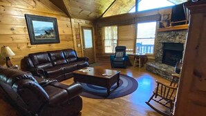 A log cabin interior with a fireplace, leather furniture, and a ceiling fan. - Hutch Mountain- This beautiful log cabin is one you will never want to leave! (Sautee Nacoochee)
