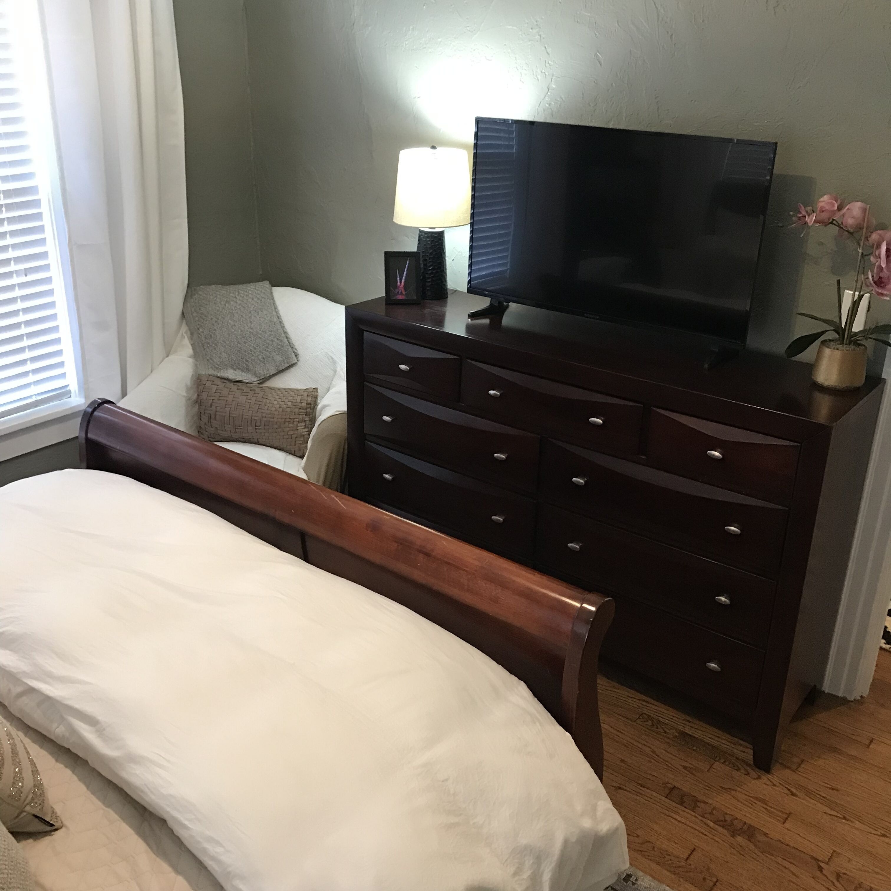 Ein Schlafzimmer mit einem Bett, einem Schminktisch, einem Fernseher und einem Fenster mit Jalousien.