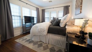A bedroom with a bed, a TV, a lamp, and a window with curtains.