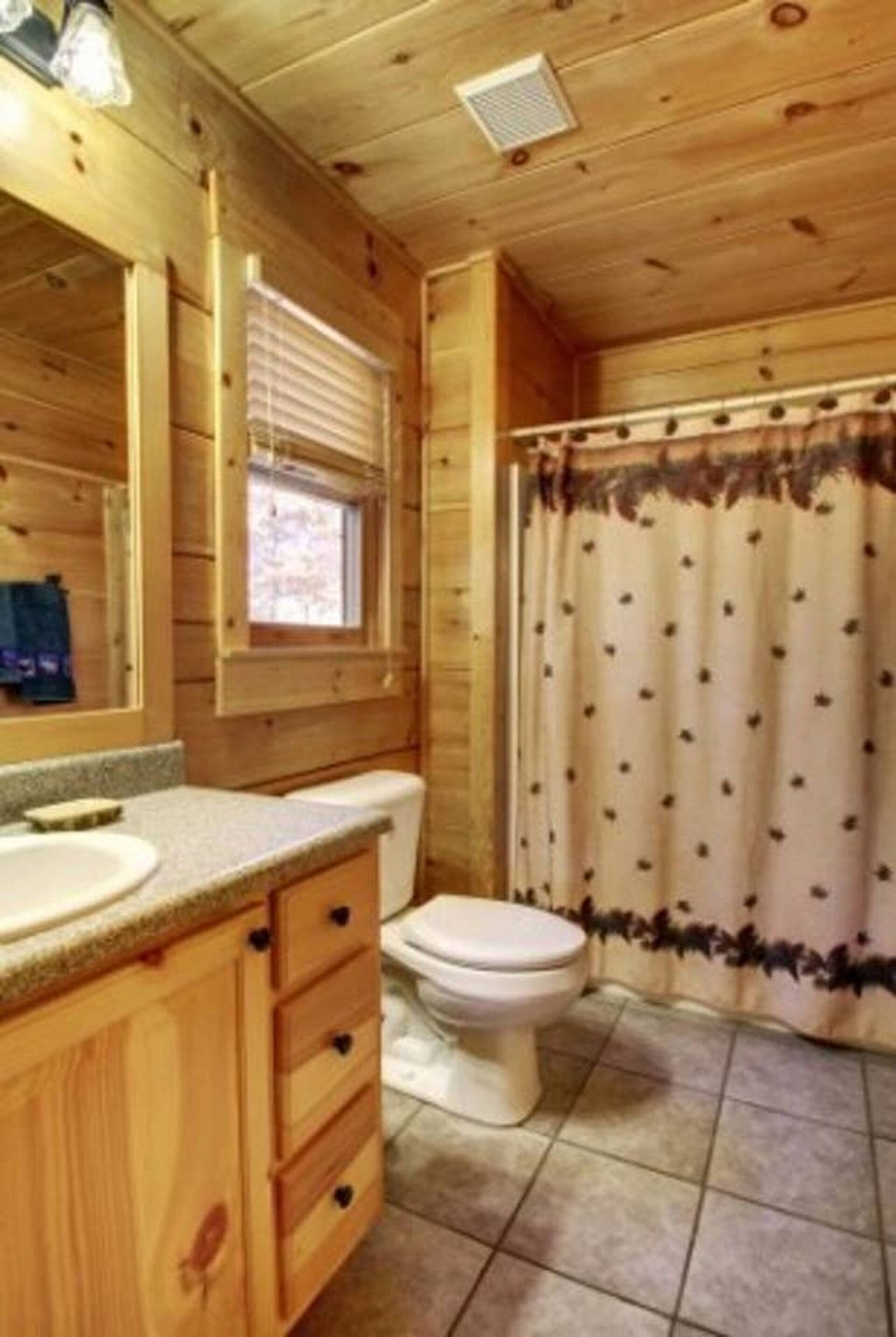 A wooden cabin bathroom with a sink, toilet, and window.
