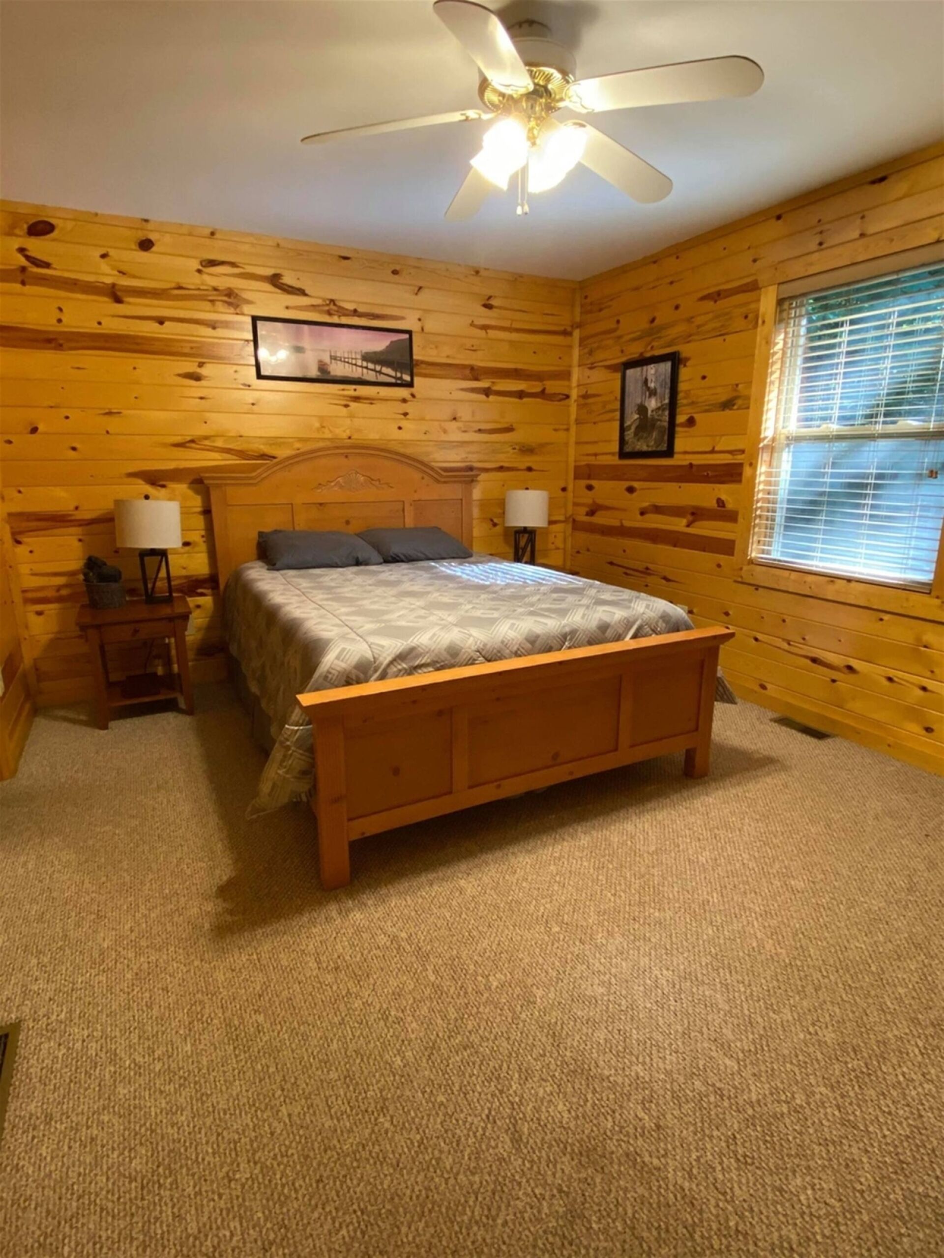 Une chambre à coucher avec un lit en bois, deux tables de chevet avec des lampes, un ventilateur de plafond et une fenêtre avec des stores.