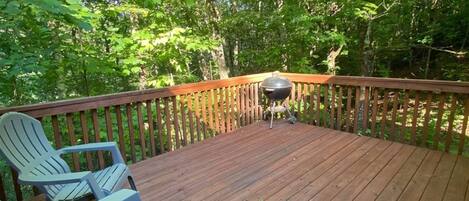 A wooden deck with Adirondack chairs, surrounded by trees.