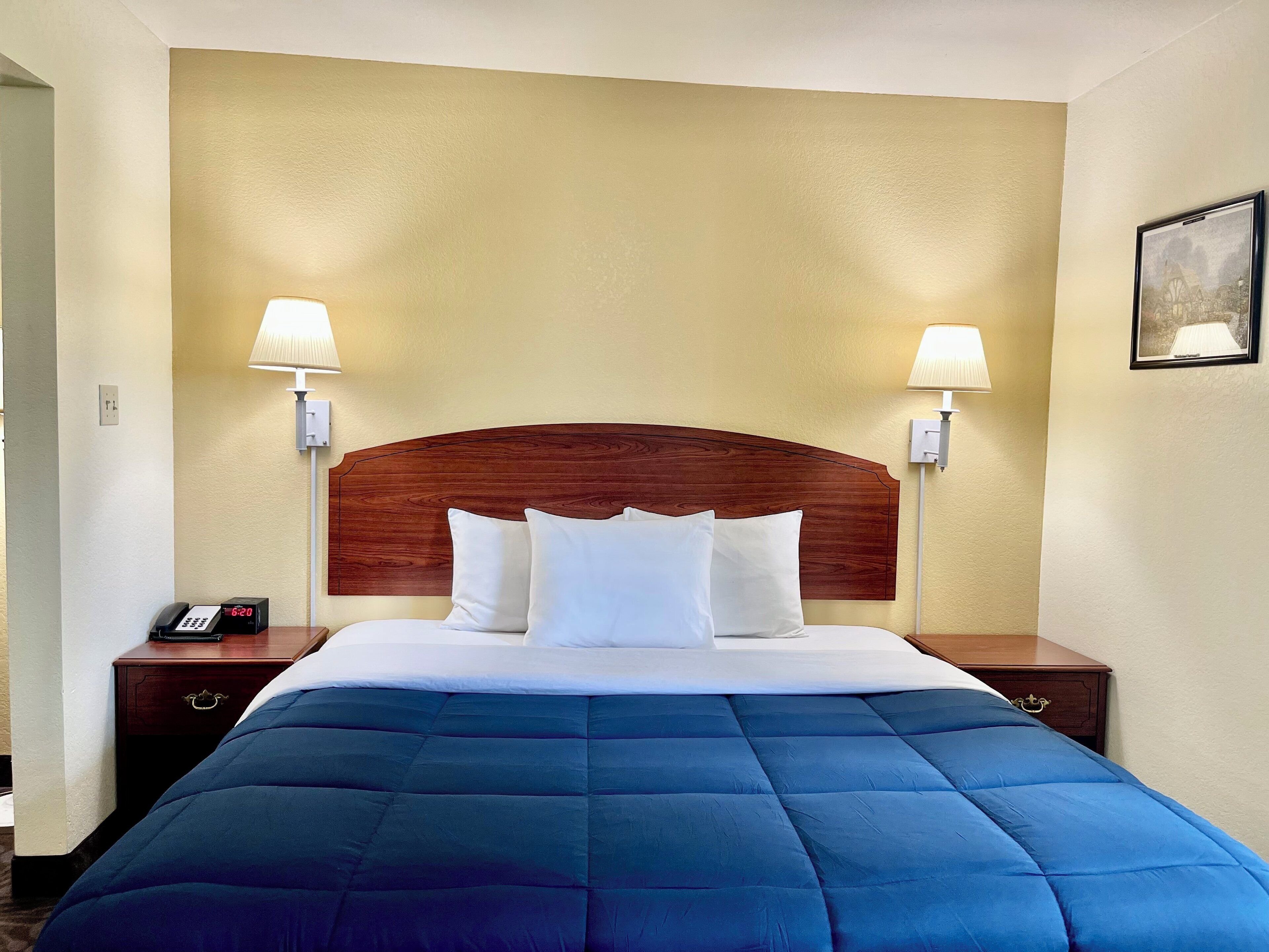 Habitación de hotel con una cama grande, dos lámparas de noche, una mesita de noche con un teléfono y un cuadro enmarcado en la pared.