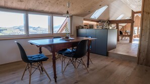 A dining area with a wooden table and chairs, a view of the countryside through large windows, and a kitchen area with a modern design. - NEW - renovated Bitzi - with a view (Appenzell)