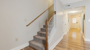 Un escalier avec des rampes en bois et des marches recouvertes de moquette, menant à un couloir doté d’un plancher en bois et de murs blancs.