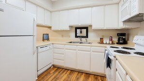 Une cuisine avec des meubles blancs, un lave-vaisselle, une cuisinière et un four à micro-ondes.