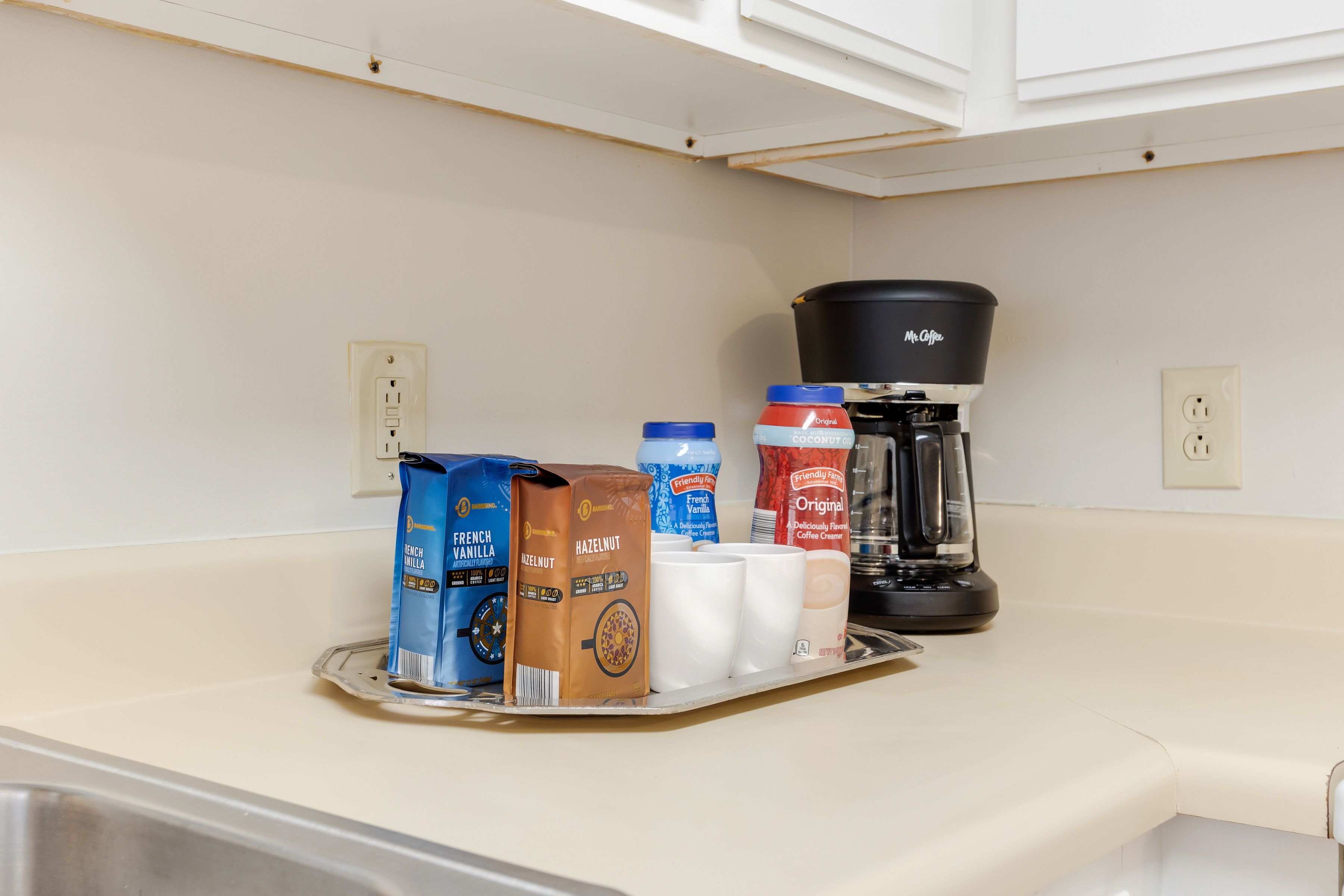 Un comptoir de cuisine avec une machine à café, un plateau contenant du lait pour café et des dosettes de café.