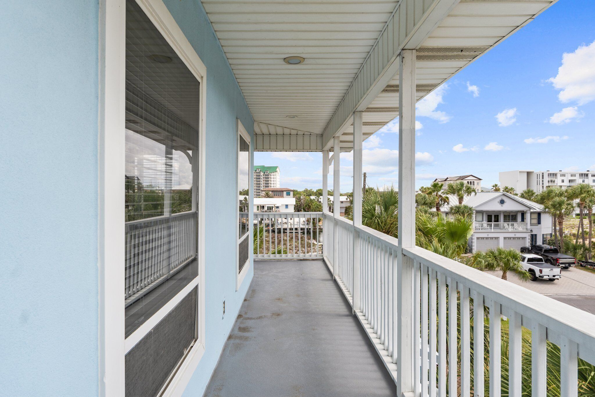 A balcony with a view of a residential area, including a white building with a garage and parked vehicles.