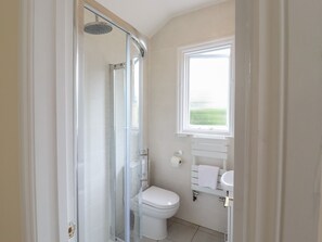 A bathroom with a glass-enclosed shower, a toilet, and a sink with a window above. - The Limes (Cambridge)