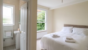 Une chambre à coucher avec un lit, une fenêtre, une porte donnant sur une salle de bain et une vue sur la verdure à l’extérieur.