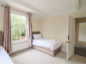 A bedroom with a single bed, a window with curtains, a radiator, and a door leading to another room. - The Limes (Cambridge)