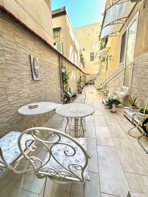 Une ruelle étroite avec deux tables rondes et des chaises, des plantes en pot et un escalier.