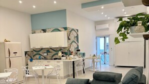 A modern living room with a grey sofa, a dining area with white chairs, and a kitchen with white cabinets and a blue accent wall. - Astonishing Studio for 2 people in the Heart of Naples 3P (Napoli)