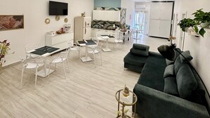 A modern living room with a dining area, a grey sofa, and a TV mounted on the wall. - Astonishing Studio for 2 people in the Heart of Naples 3P (Napoli)