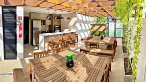 An outdoor dining area with wooden tables and chairs, a kitchen with modern appliances, and a fire extinguisher mounted on the wall. - Vacanze - Smart (Maceió)