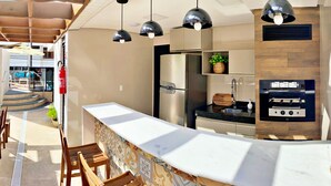 A modern outdoor kitchen with a marble countertop, stainless steel appliances, and pendant lighting. - Vacanze - Smart (Maceió)