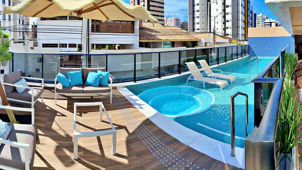 A rooftop pool area with lounge chairs, a sofa, and a wooden deck. - Vacanze - Smart (Maceió)