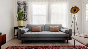 A living room with a grey sofa, two cushions, a patterned rug, a floor lamp, and a plant. - 5 mins to best of ATX, Stocked kitchen, 4BR 2.5BA, Backyard, Grill, yard games (Austin)