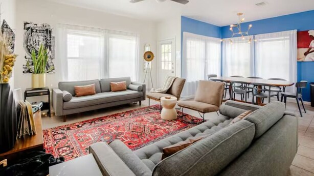 A modern living room with a grey sofa, a red patterned rug, and a dining area with a table and chairs. - 5 mins to best of ATX, Stocked kitchen, 4BR 2.5BA, Backyard, Grill, yard games (Austin)
