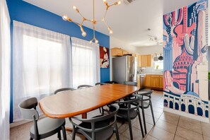 A dining area with a wooden table and chairs, a modern chandelier, and a colorful mural on the wall. - 5 mins to best of ATX, Stocked kitchen, 4BR 2.5BA, Backyard, Grill, yard games (Austin)