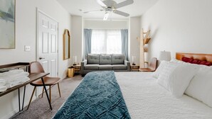 A hotel room with a bed, a sofa, a desk, a chair, a ceiling fan, and a window with curtains. - 5 mins to best of ATX, Stocked kitchen, 4BR 2.5BA, Backyard, Grill, yard games (Austin)