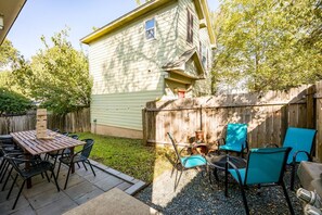 A backyard with a wooden table and chairs, a wooden fence, and a house with a chimney. - 5 mins to best of ATX, Stocked kitchen, 4BR 2.5BA, Backyard, Grill, yard games (Austin)