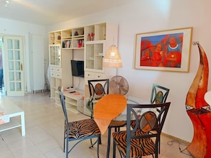 A dining area with a glass table, zebra-striped chairs, a white cabinet with shelves, a television, and a painting on the wall.
