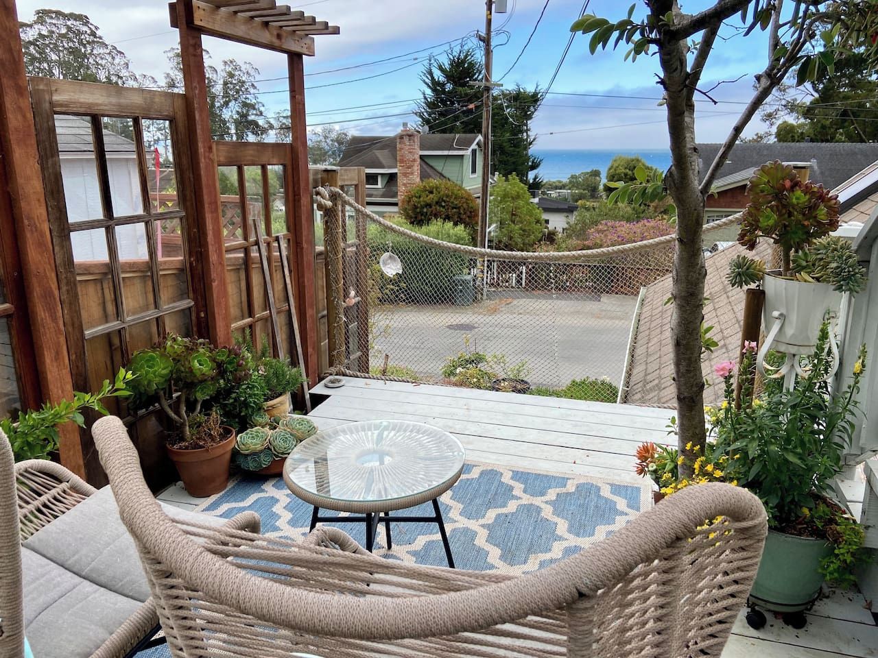 Une terrasse avec des meubles en osier, une table en verre et des plantes en pot.