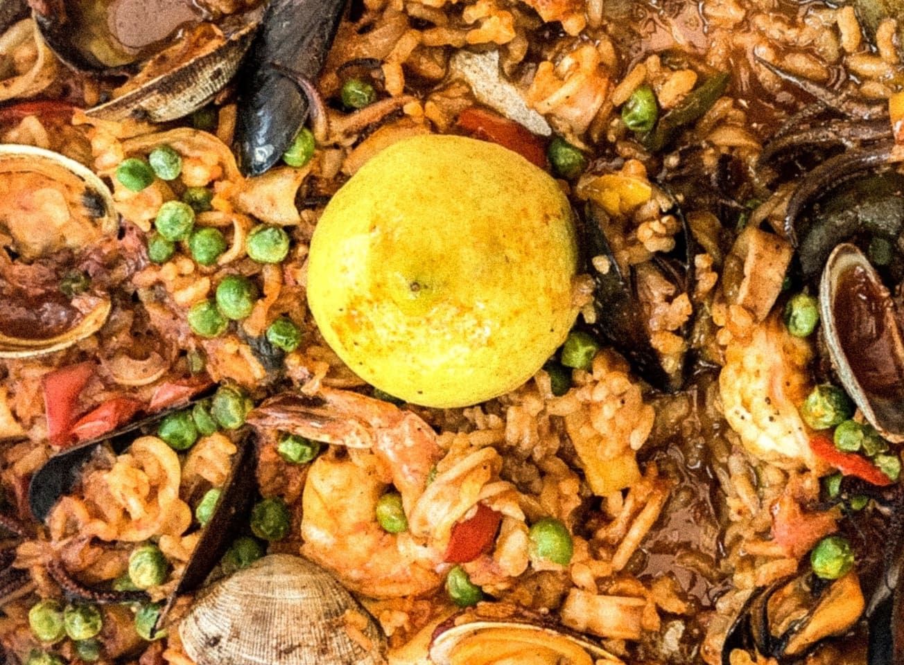 Primer plano de una paella de mariscos con guisantes y una rodaja de limón.