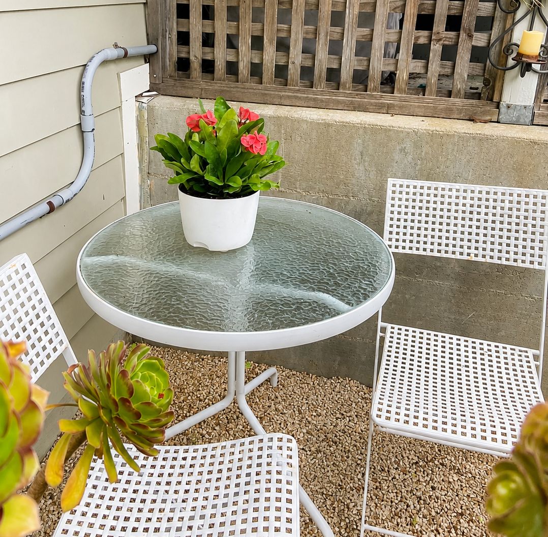 A round glass table with a potted plant and two white metal chairs.