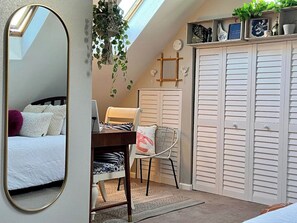 Une chambre avec un puits de lumière, un bureau avec une chaise, une armoire et une plante suspendue.