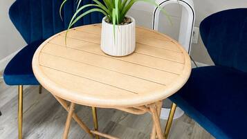 A round wooden table with a white pot containing a plant, flanked by two blue chairs with gold legs, on a light-colored wooden floor.