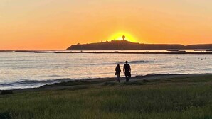 Ein Sonnenuntergang über einem Gewässer, zwei Personen spazieren am Ufer entlang.