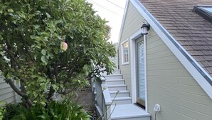 Et hus med en lille veranda, et træ med grønne blade og en lysegrå facade.