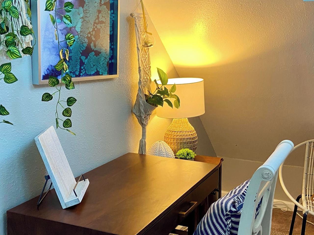 A corner of a room with a wooden desk, a lamp, a chair, and a wall-mounted plant.