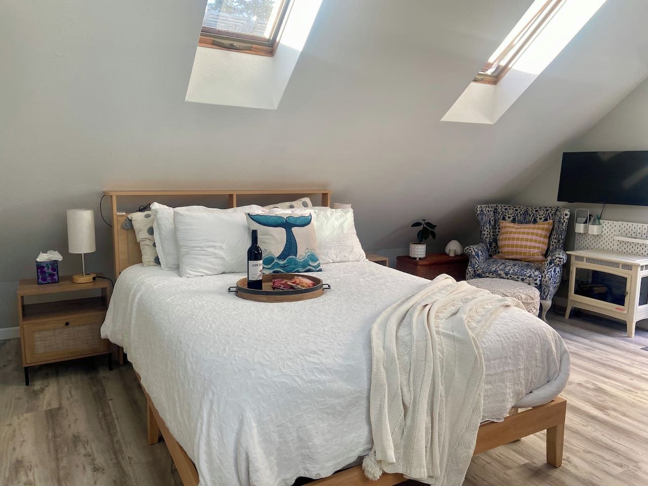 A bedroom with a large bed, a bedside table, a chair, a TV, and skylights.