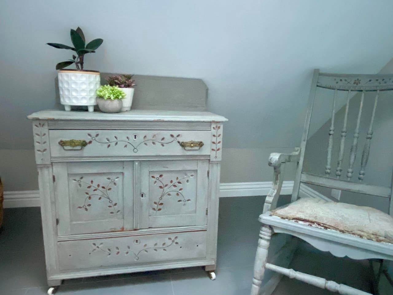 A white dresser with floral patterns and two potted plants on top.