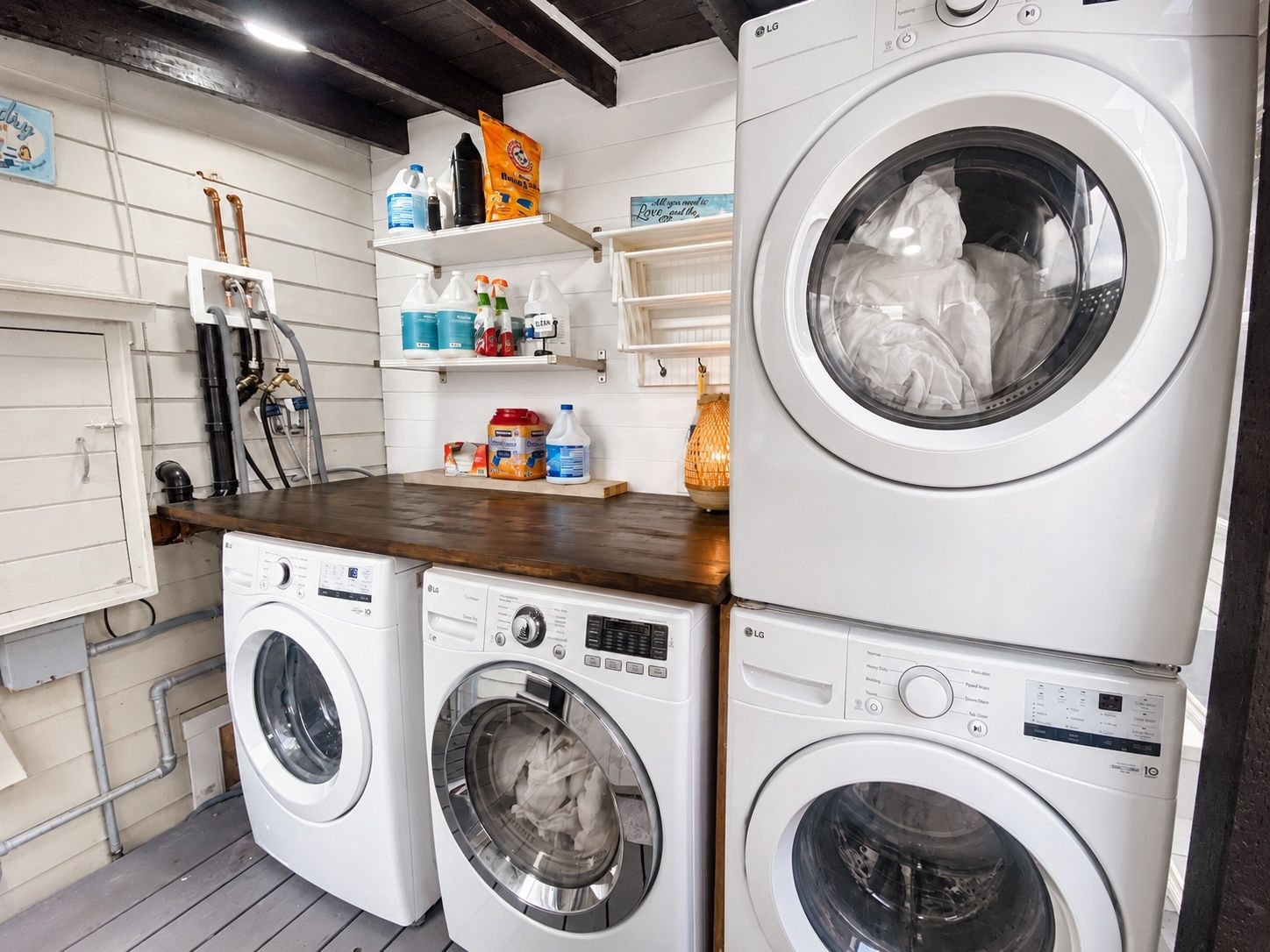 A laundry room with two stacked LG washing machines, shelves with cleaning supplies, and a wooden countertop.