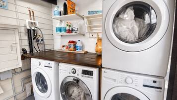 A laundry room with two stacked LG washing machines, shelves with cleaning supplies, and a wooden countertop.