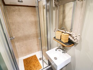 Un baño con ducha envuelta en vidrio, un lavamanos blanco y un espejo con detalles ornamentales.