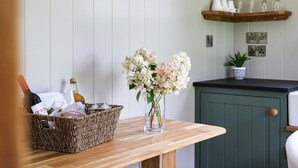 A kitchen with a wooden table, a wicker basket, a vase with flowers, and a green cabinet. - Little Silver Pheasant (Umberleigh)