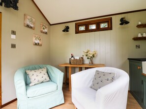 Una habitación acogedora con un sillón azul claro y un sillón blanco, una pequeña mesa de madera con un jarrón de flores y un mueble de madera.