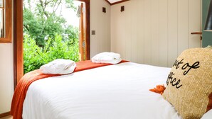 A bedroom with a large bed, a view of greenery through an open door, and a ceiling with wooden beams. - Little Silver Pheasant (Umberleigh)