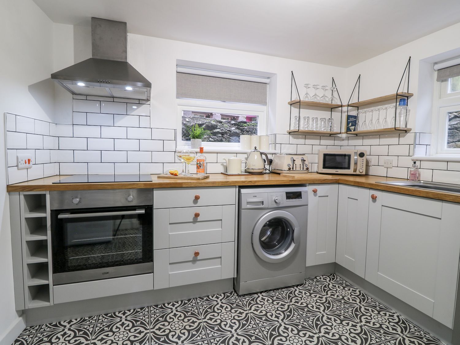 A compact kitchen with a built-in oven, microwave, and washing machine, white cabinetry, and a patterned floor.